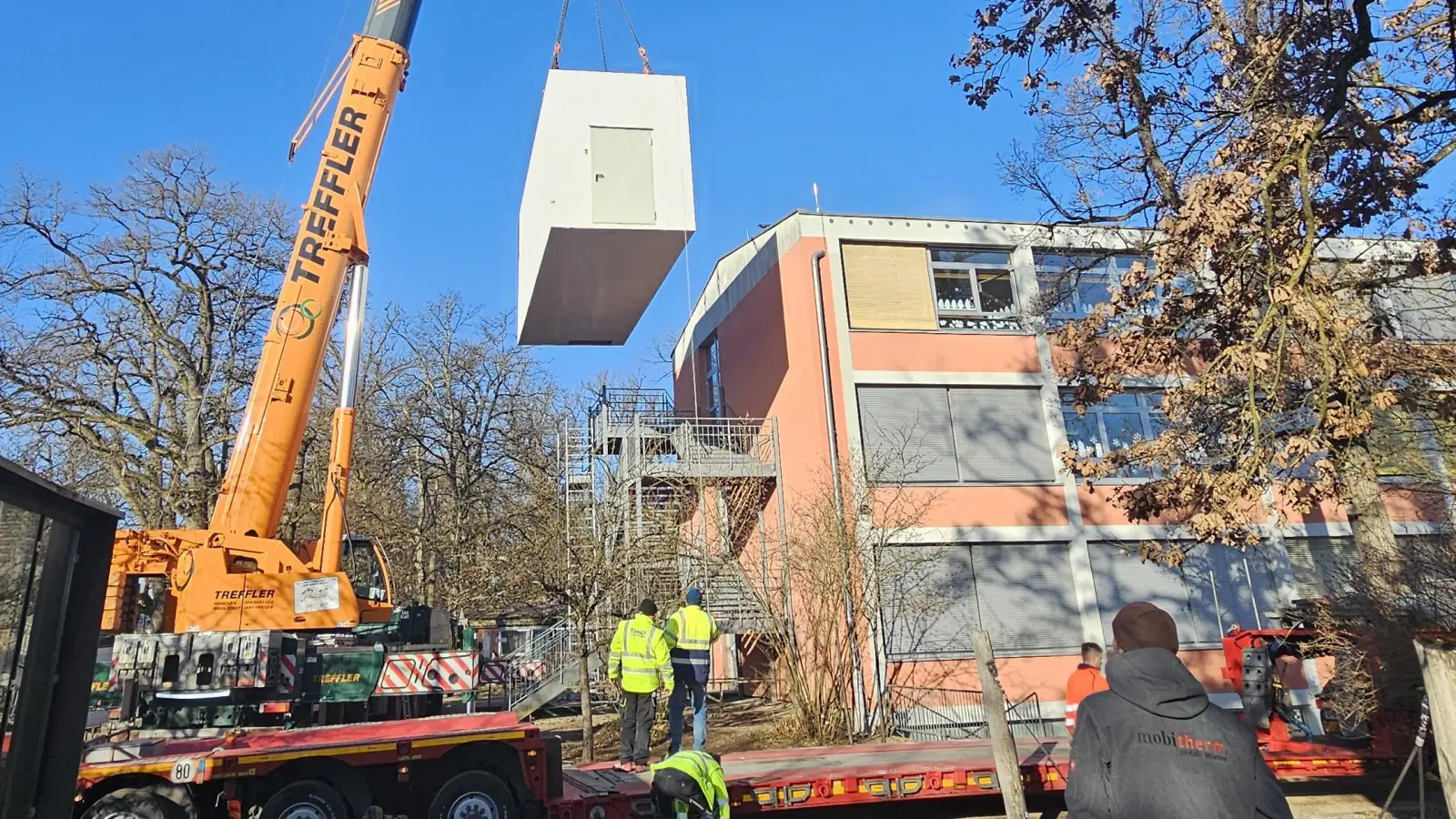 Der Autokran hebt das erste Betonmodul an seinen zukünftigen Standort neben der Grundschule Krailling. In den kommenden Wochen wird hier die neue Pelletheizung installiert. (Foto: Gemeinde Krailling)