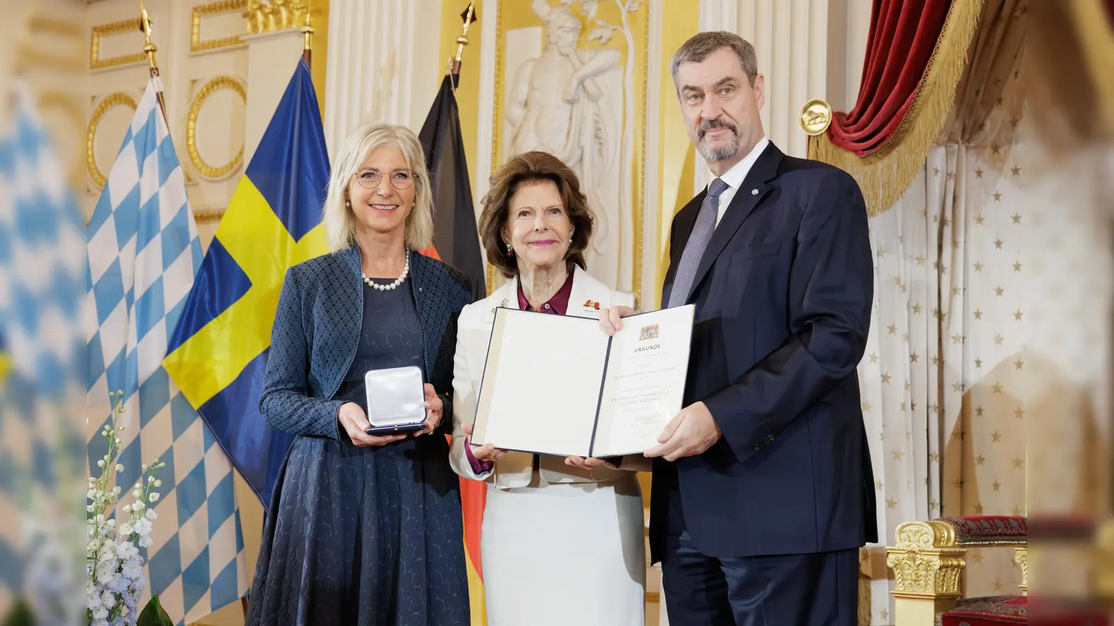 Sozialministerin Ulrike Schaf (l.) und Ministerpräsident Markus Söder überreichten die Sozialmedaille an Königin Silvia von Schweden. (Foto: Martina Nötel)
