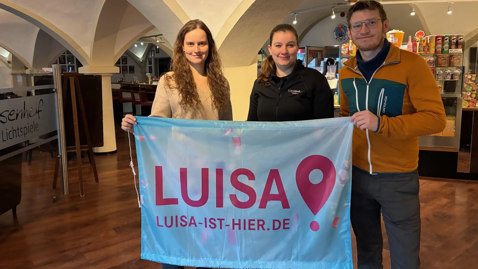 Katharina von Schumann von der kommunalen Jugendarbeit am Landratsamt Freising (v.l.) freut sich, dass die Rosenhof-Lichtspiele, hier mit Geschäftsführerin Verena Dollinger und dem technischen Betriebsleiter Kilian Stackelberg, die Kampagne „LUISA IST HIER!“ einführen. (Foto: LRA Freising)