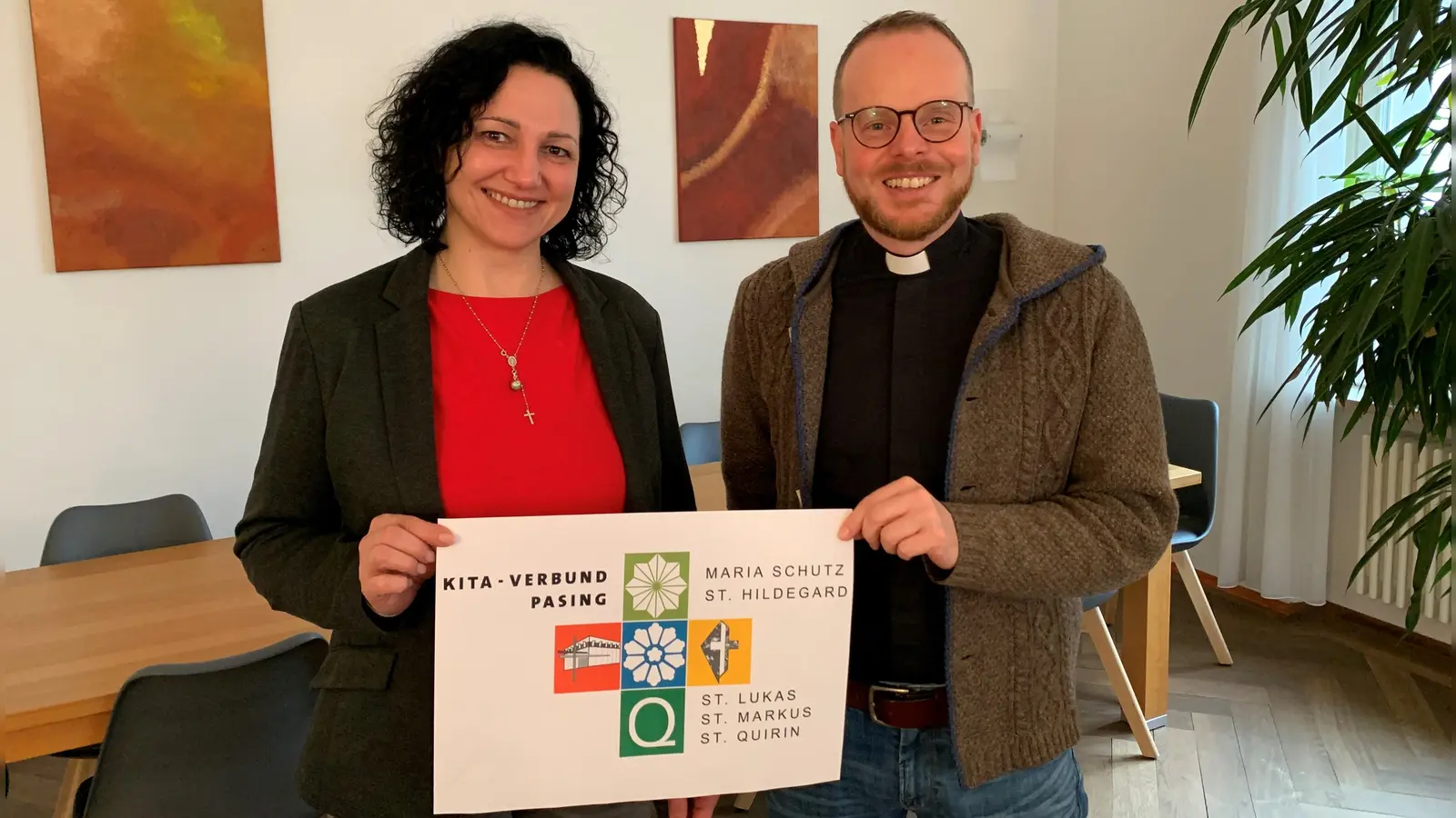 Kita-Verbund-Verwaltungsleiterin Anica Baranyi und Pfarrer Alois Emslander, Pfarradministrator der Pfarrei Maria Schutz, mit dem neuen Logo des Kita-Verbunds Pasing, das alle fünf Einrichtungen zeigt. (Foto: Johannes Stöber)