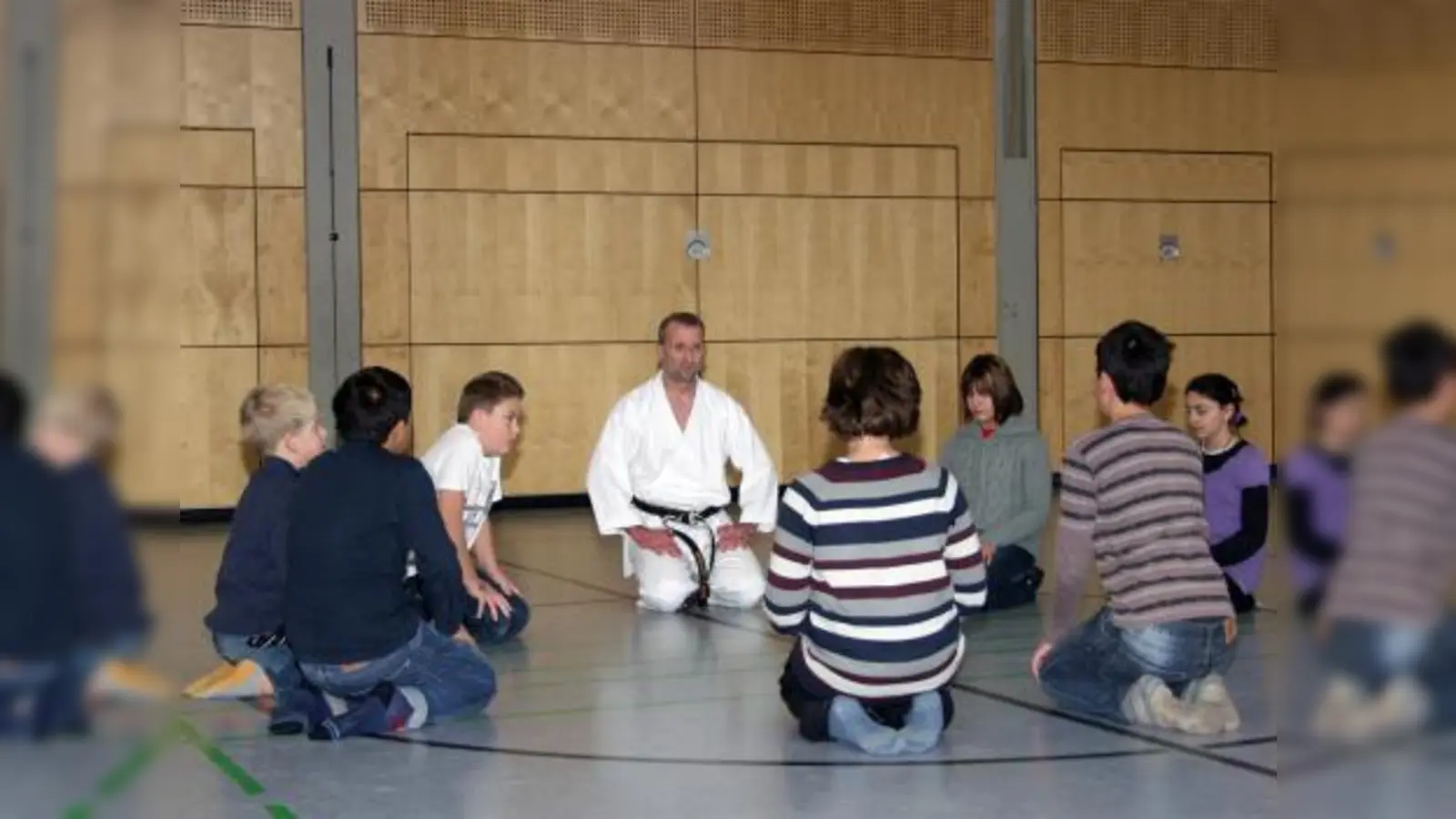 Nachdem sich die Schülerinnen und Schüler kurz in der Turnhalle ausgetobt haben, sammeln sie sich zum Beginn der Karatestunde mit ihrem Trainer zu einer Konzentrationsübung im Kreis. (Foto: Eva Schraft)